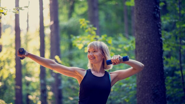 Photo fit young blonde woman working out with dumbbells outside