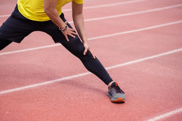 Fit young man warms up leg muscles on rubber running track at sports ground in urban park