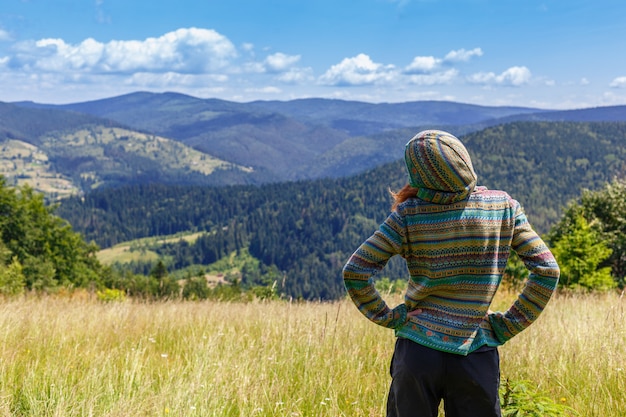 Fit young woman hiking in the mountains standing on a rocky summit ridge with backpack and pole looking out over an alpine landscape