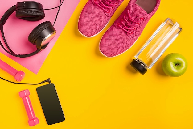 Fitness accessories on yellow background. Sneakers, bottle of water, headphones and smart. Top view. Still life. Copy space