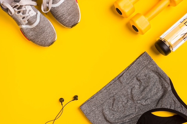 Fitness accessories on a yellow background sneakers bottle of water headphones and sport top