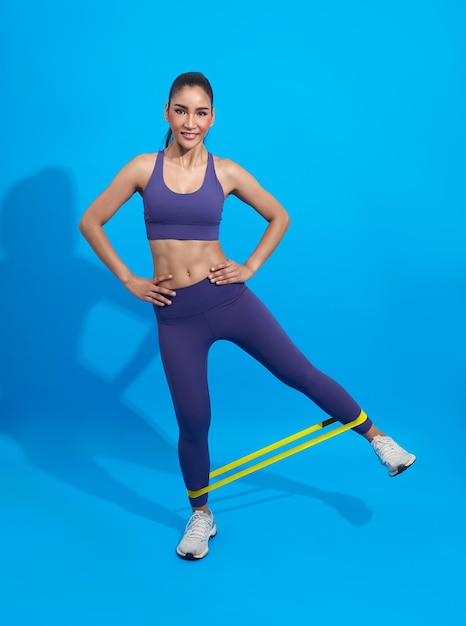 Fitness asian woman doing exercise for glute with resistance band on blue background