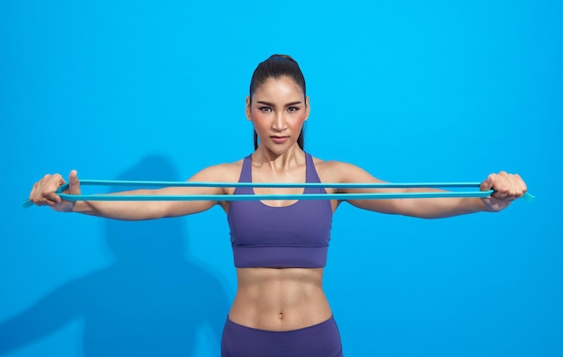 Fitness asian woman in sportswear exercising with a resistance band on blue background