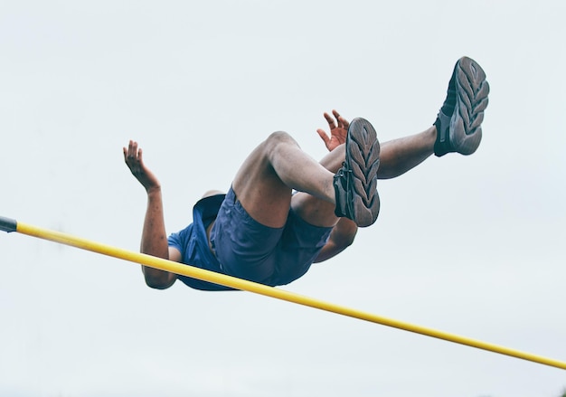 Fitness athletics high jump by man at a stadium for training energy and cardio against sky background Jumping athlete and male outdoors for performance endurance and competition on mock up