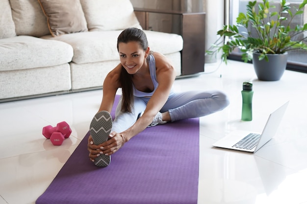 Fitness beautiful slim woman doing fitness stretching exercises at home in the living room. Stay at home activities. Sport, healthy lifestyle.