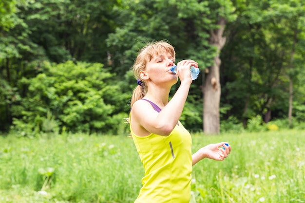 Fitness beautiful woman drinking water and sweating after exercising on summer hot day. Female athlete after work out.