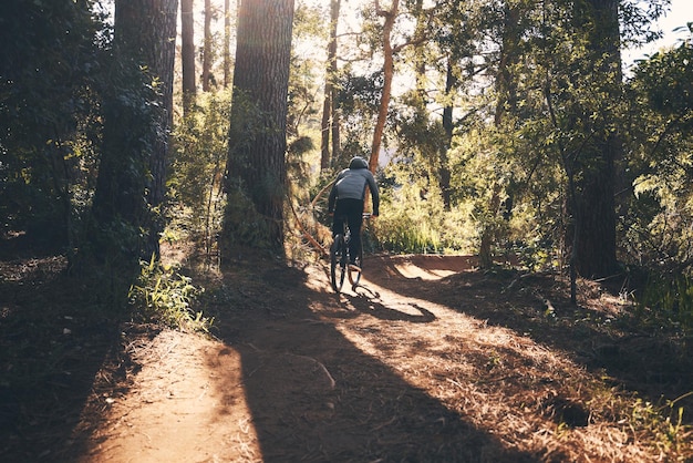 Photo fitness bicycle and man back outdoor on a forest path with extreme and exercise adventure bike cycling and sport of an athlete with fast speed and nature cycle for sports training and race action