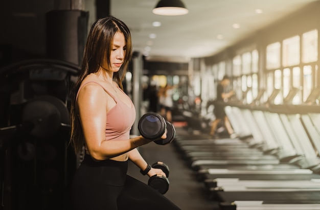 Fitness concept, beautiful Asian woman lifting dumbbells to build muscle in fitness gym.