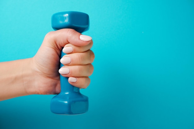 Fitness concept A female hand holds a blue plastic dumbbell Blue background