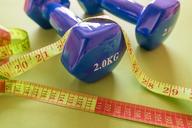 Fitness concept Photo of a tape measure and dumbbells on an isolated green background