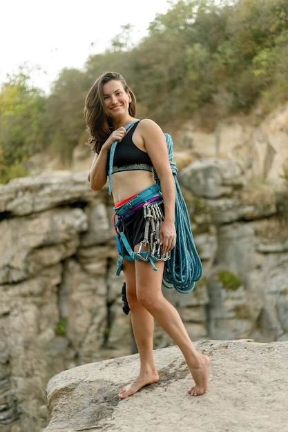 Fitness, extreme sport and healthy lifestyle concept - Climber holds the rope. Slender girl holds climbing equipment at a rock wall. and looking at camera on background of rock