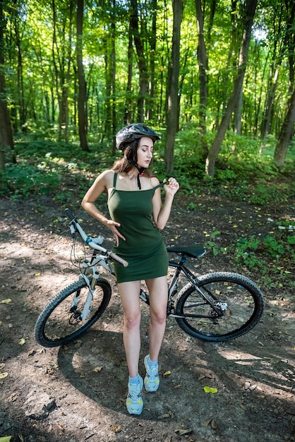 Fitness girl wear green dress rides a modern mountain bike in forest at hot summer day Activity freedom and relaxation lifestyle