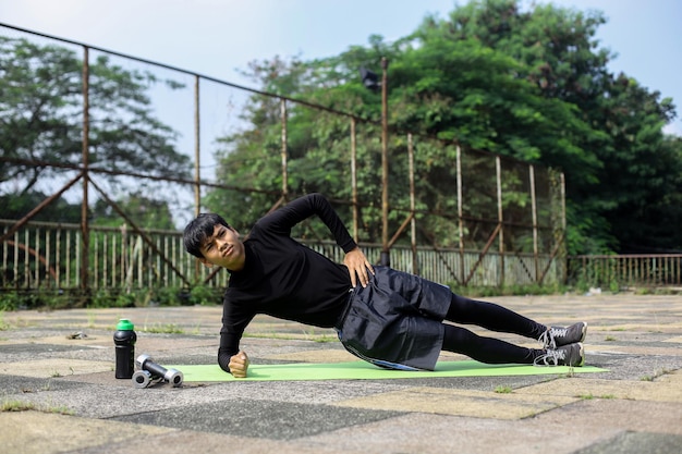 Fitness guy doing side plank workout on a mat at outdoors