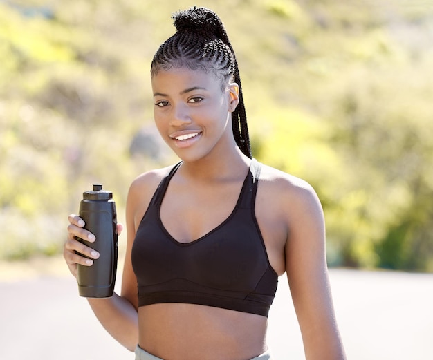 Fitness health and sports with black woman and bottle for running exercise or training in the outdoor Motivation workout and water with portrait of young girl or runner in nature for wellness