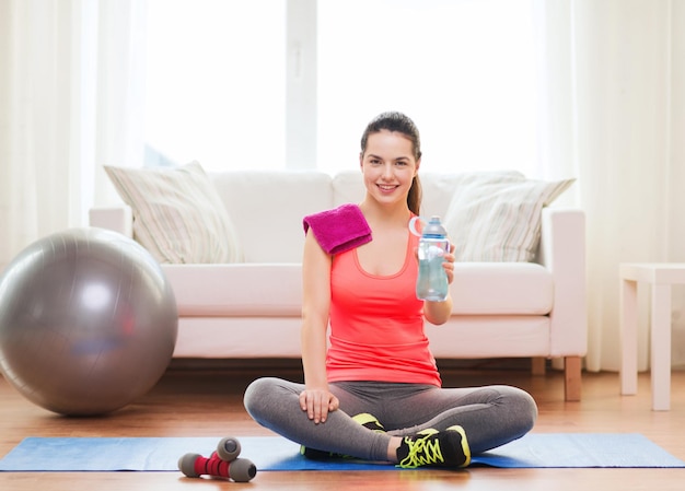 fitness, home and diet concept - smiling teenage girl with bottle of water after exercising at home