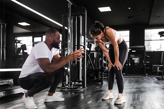 Fitness instructor exercising with his client at the gym african man and caucasian woman