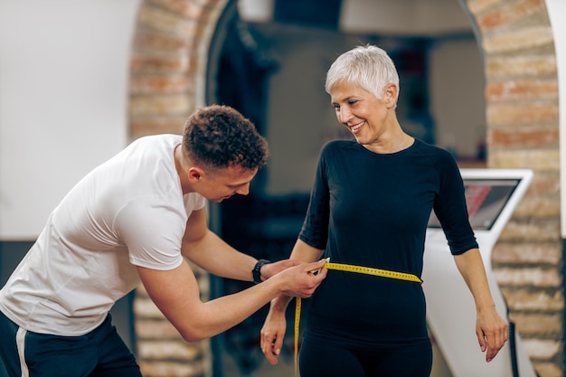 Fitness instructor measuring senior woman's waist before working out in the gym.