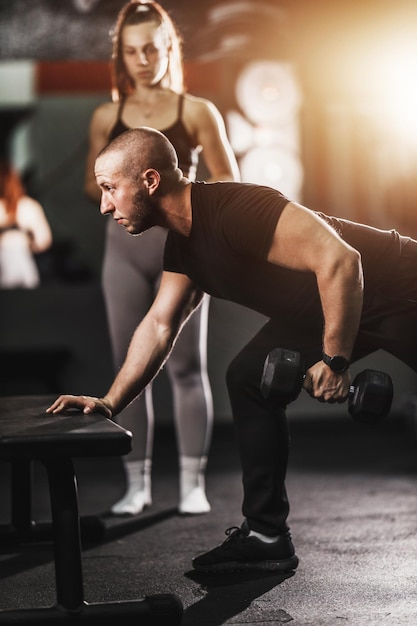 Fitness instructor showing exercise for back muscle to a fit young woman at the training in a gym.