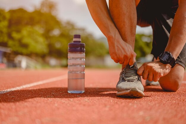 Fitness, jogging, running, exercise, lifestyle and healthy concept. The young man are using their hands to tie their shoes for jogging on the running track around the football field.