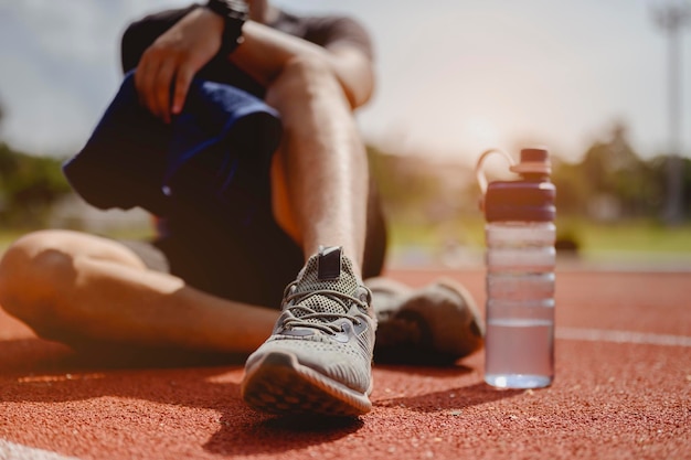 Fitness, jogging, running, exercise, lifestyle and healthy concept. The young man wore all parts of his body and drink water to prepare for jogging on the running track around the football field.