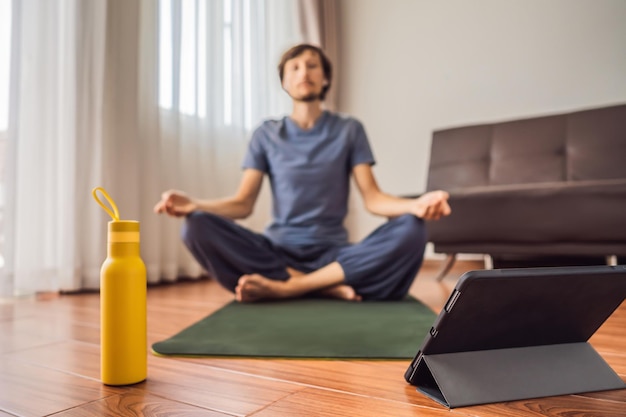 Fitness man exercising on the floor at home and watching fitness videos in a tablet People do sports online because of the coronovirus