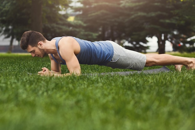 Fitness man plank workout training in park outdoors. Young guy makes exercise. Healthy lifestyle, gymnastics concept