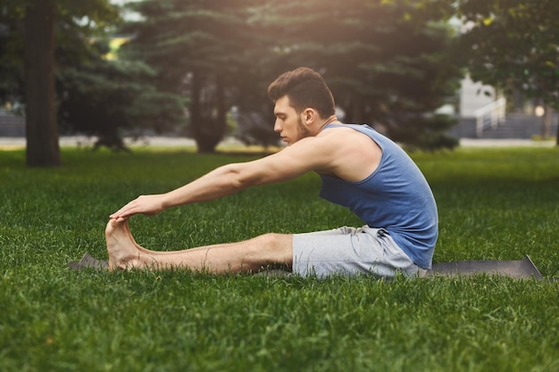 Fitness man at stretching training outdoors. Young sporty guy makes aerobics exercise in park. Healthy lifestyle, gymnastics concept