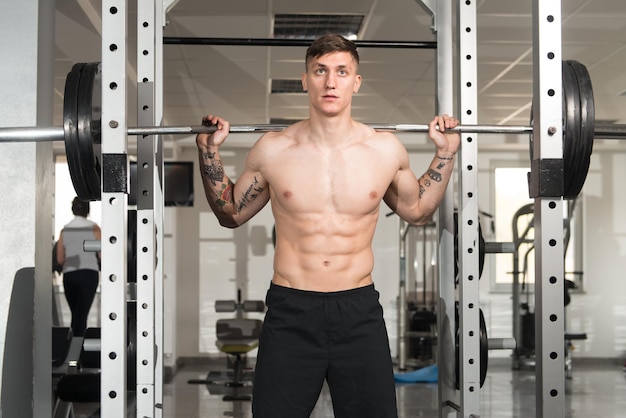 Fitness Man Using Barbell Exercising Legs Inside Gym