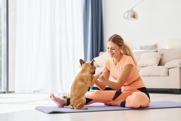 On fitness mat Woman with pug dog is at home at daytime