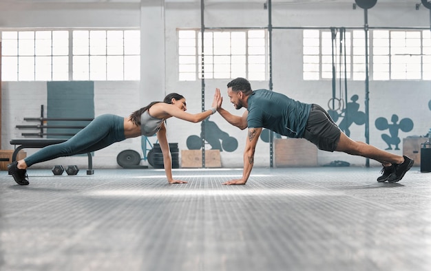 Fitness partners exercising together and doing pushups high five at the gym Fit and active man and woman training in a health facility as part of their workout routine A couple doing an exercise