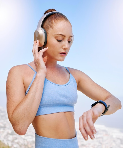 Photo fitness runner and woman on time by her smartwatch as she monitors her performance heartbeat and pulse outdoors headphones health and girl running in summer streaming music radio song or podcast