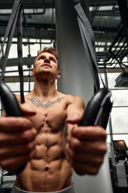 Fitness, sport, bodybuilding and people concept - young man doing push-ups on gymnastic rings in gym.