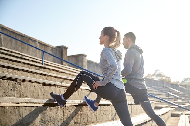 fitness, sport, exercising and lifestyle concept - couple stretching leg on stands of stadium