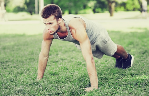 fitness, sport, exercising, training and lifestyle concept - young man doing push ups or plank exercise on grass in summer park