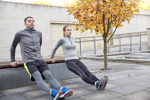 fitness, sport, exercising, training and people concept - couple doing triceps dip exercise on city street bench