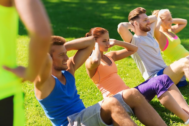 Photo fitness, sport, friendship and healthy lifestyle concept - group of happy teenage friends or sportsmen exercising and doing sit-ups at boot camp