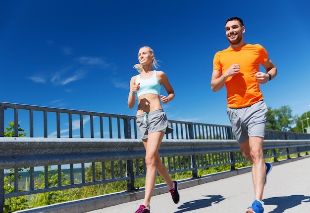 fitness, sport, friendship and healthy lifestyle concept - smiling couple running at summer seaside