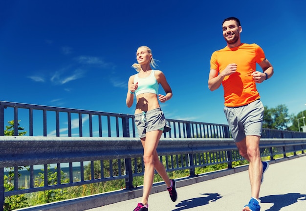 fitness, sport, friendship and healthy lifestyle concept - smiling couple running at summer seaside