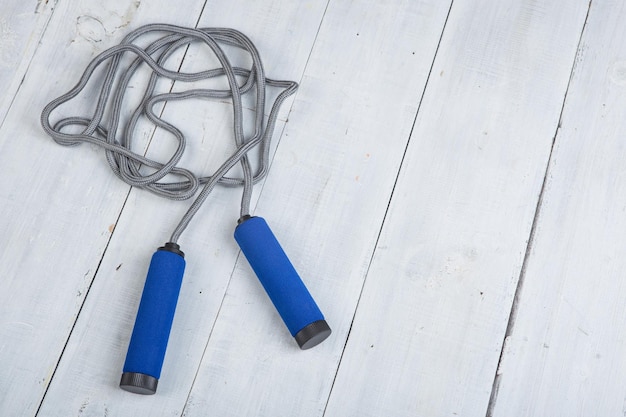 Photo fitness/sport and healthy lifestyle concept - jumping/skipping rope with blue handles on white wooden background