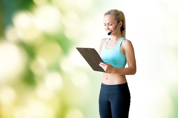 fitness, sport and people concept - happy woman sports trainer with microphone and clipboard over green natural background