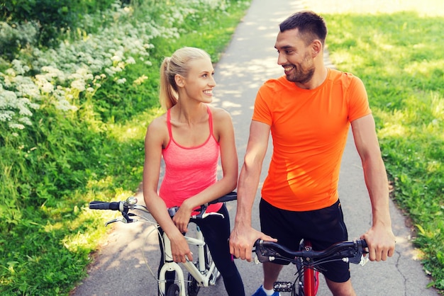 fitness, sport, people and healthy lifestyle concept - happy couple riding bicycle outdoors at summer