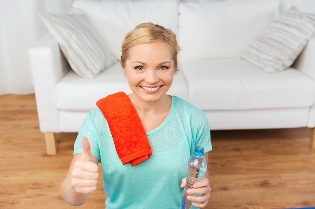 fitness, sport, people and healthy lifestyle concept - happy woman with bottle of water after exercising at home and showing thumbs up