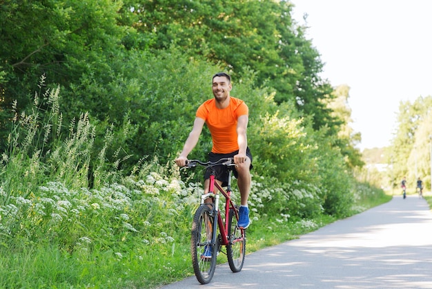 fitness, sport, people and healthy lifestyle concept - happy young man riding bicycle outdoors