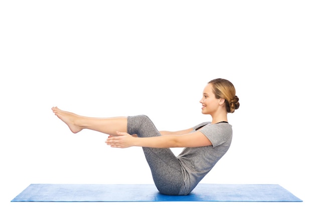 fitness, sport, people and healthy lifestyle concept - woman making yoga in half-boat pose on mat