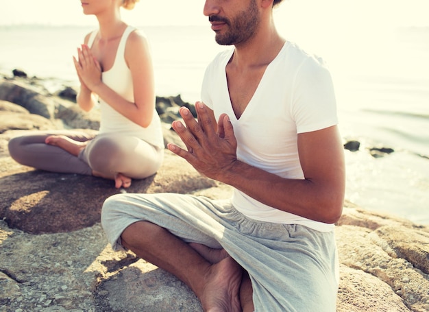 fitness, sport, people and lifestyle concept - close up of couple making yoga exercises sitting on pier outdoors