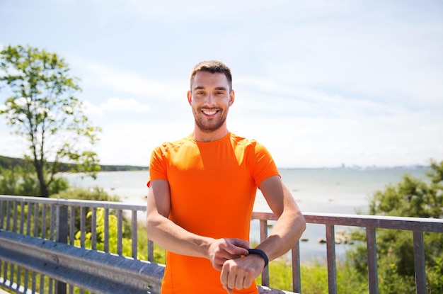 fitness, sport, people, technology and healthy lifestyle concept - smiling young man with smart wristwatch at summer seaside