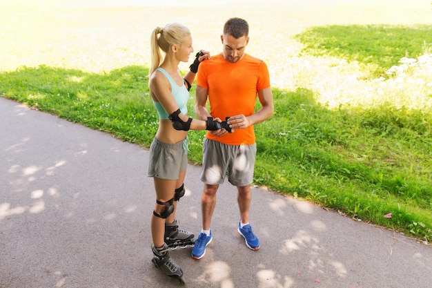 fitness, sport, summer and healthy lifestyle concept - happy couple with roller skates riding outdoors