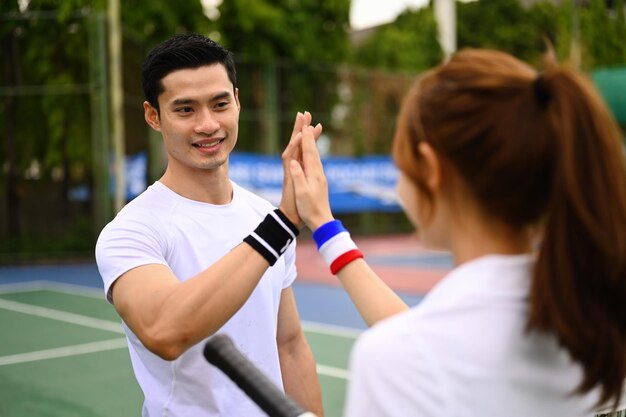 Fitness sport tennis couple giving each other a high five while playing tennis together on a court