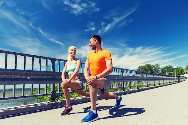 fitness, sport, training and lifestyle concept - smiling couple stretching outdoors