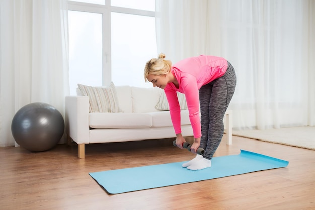 fitness, sport, training and lifestyle concept - smiling woman with dumbbells exercising and doing lean at home